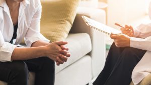 A therapist holding a clipboard gestures as their client sits across from them. This could represent trauma therapy in Colorado Springs, CO. Contact a trauma therapist to learn more about posttraumatic stress disorder in Colorado and other services. 