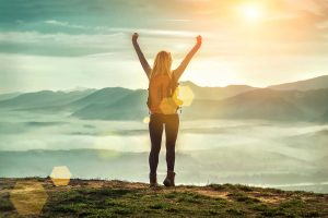 A woman on top of a mountain raises her hands in victory. This could represent overcoming posttraumatic stress disorder in Colorado. Contact a trauma therapist in Colorado Springs, CO for support with trauma therapy and other services. 