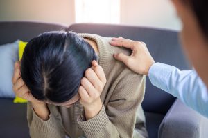 A woman hangs her head as a person places a supportive hand on her shoulder. This symbolizes support from counseling in Colorado Springs, CO. Contact a therapist in Colorado Springs, CO or an online marriage counselor in Colorado for more information.