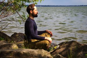 A man sits with eyes closed next to the open water. This represents the inner peace that faith-based counseling in Colorado Springs, CO can provide. Contact a faith-based counselor in Colorado today for more information!