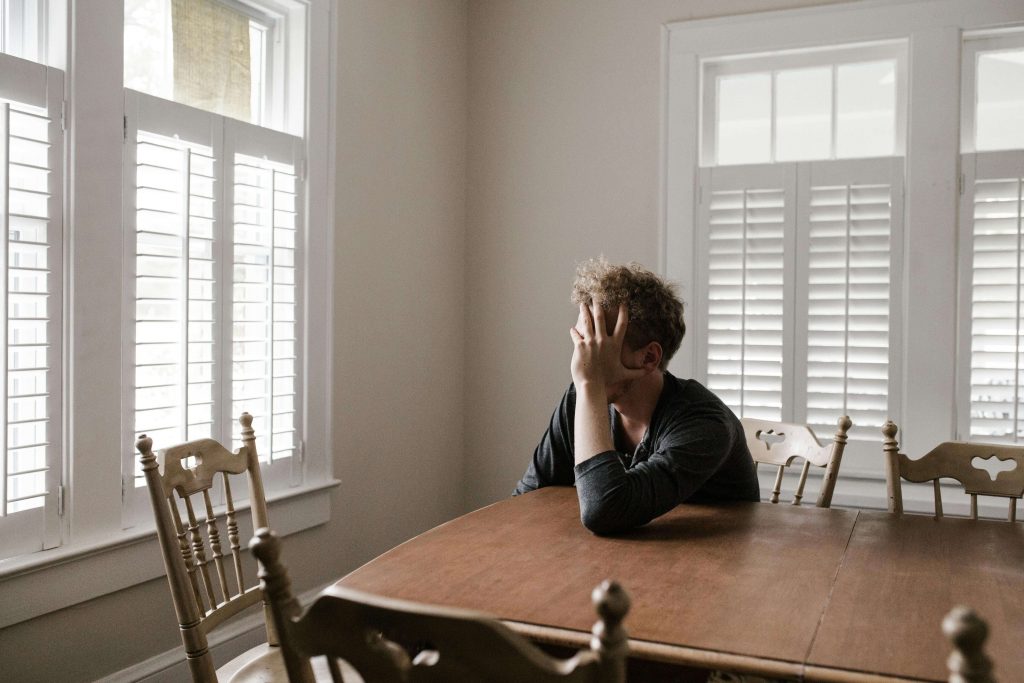 Man sitting alone at a table with his head in his hand, reflecting stress and anxiety, representing online anxiety counseling for men in Colorado Springs, CO.