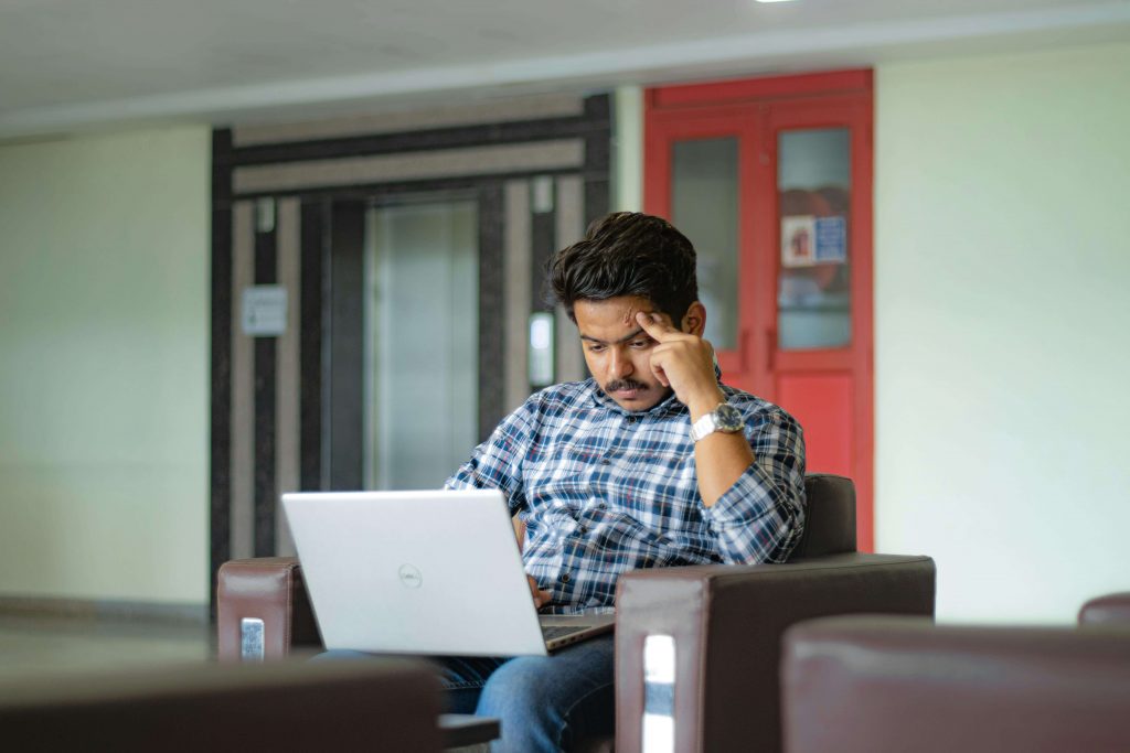 Man sitting with a laptop, looking thoughtful and stressed, illustrating the search for a therapist for men in Colorado Springs, CO.