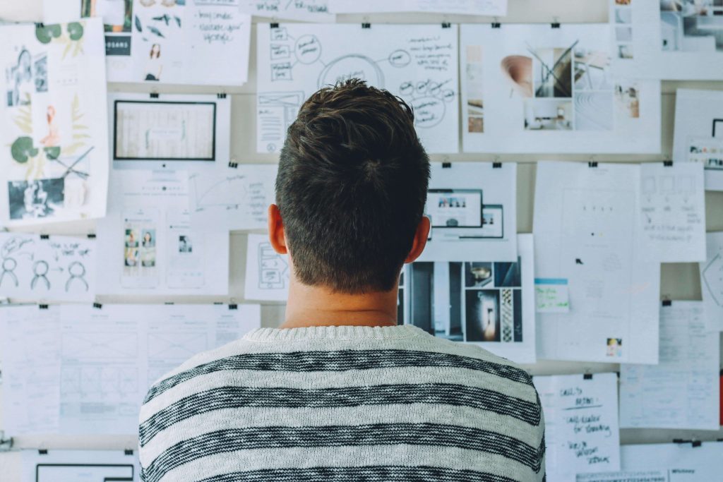 Man standing and facing a wall of notes and ideas, representing mental overload, problem-solving pressure, and men’s therapy for stress in Colorado Springs, CO.