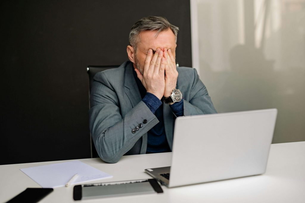 Man sitting at a desk with his face in his hands, reflecting unexpressed grief and emotional pressure often addressed through grief counseling for men in Colorado Springs, CO.