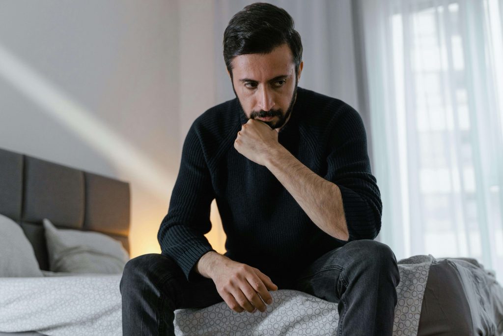 Man sitting on the edge of a bed looking down thoughtfully, representing self-reflection supported by therapy for breaking cycles in Colorado Springs, CO.