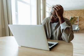 Man looking stressed while using a laptop, illustrating daily responsibilities managed alongside healing in childhood trauma therapy in Colorado Springs, CO.