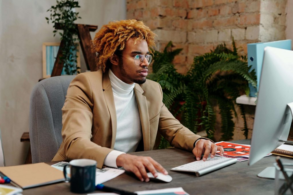 Man wearing a turtleneck and glasses looking stressed while using a computer at work, representing challenges addressed in therapy for imposter syndrome in Colorado Springs, CO.
