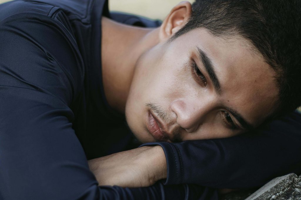 Man resting his head on a table with an emotional expression, illustrating struggles addressed in masculinity and mental health in Colorado Springs, CO.