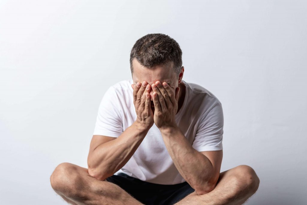 Man sitting on the ground covering his face with his hands, representing struggles addressed in men’s therapy for emotional withdrawal in Colorado Springs, CO.