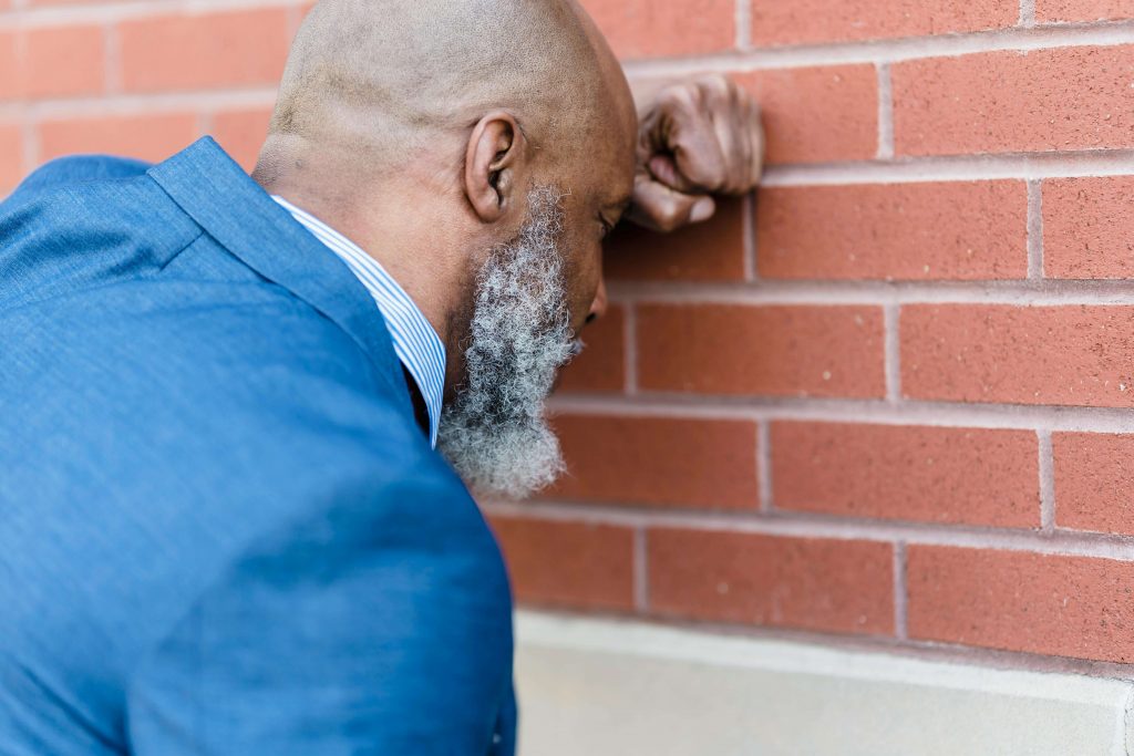 Man leaning toward a brick wall with his fist resting against it, looking stressed, illustrating overwhelm addressed in stress management therapy for men in Colorado Springs, CO.