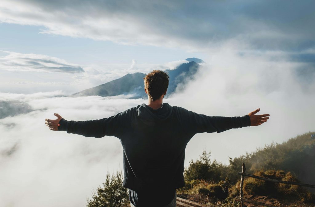 Man standing with his arms outstretched in front of a mountain view, symbolizing healing and openness through men’s therapy for emotional withdrawal in Colorado Springs, CO.