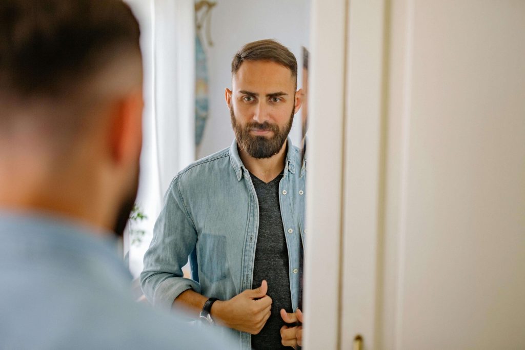 Man looking at his reflection in a mirror, illustrating self-evaluation and fear of failure addressed in therapy for perfectionistic men in Colorado Springs, CO.