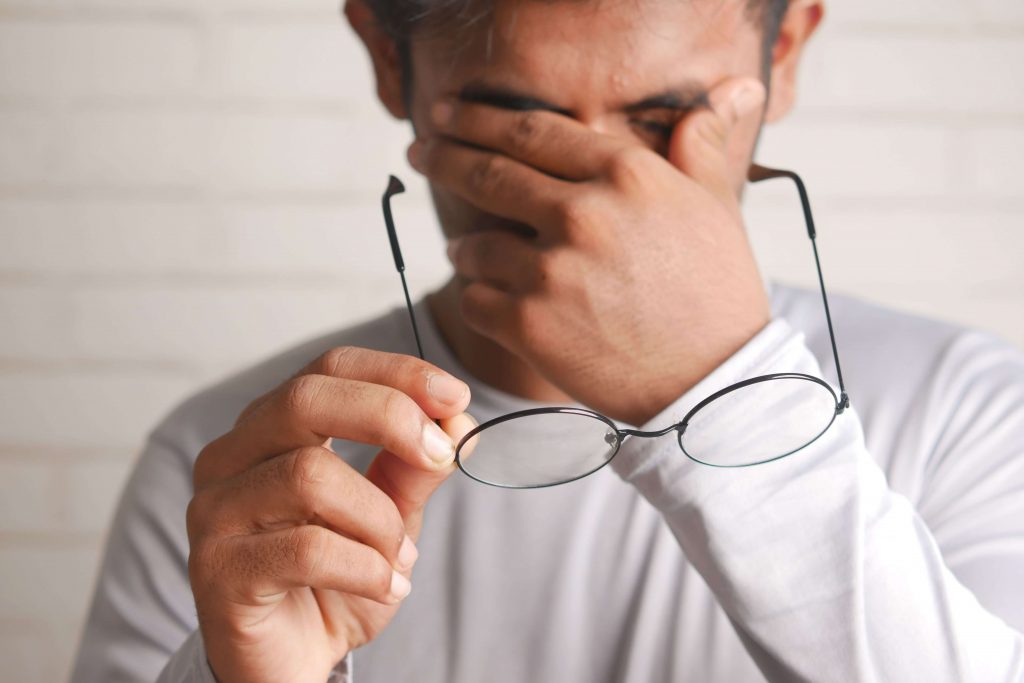 Man taking off his glasses with his hand on his face, appearing anxious, representing the lingering effects of trauma addressed through EMDR therapy for men in Colorado Springs, CO.